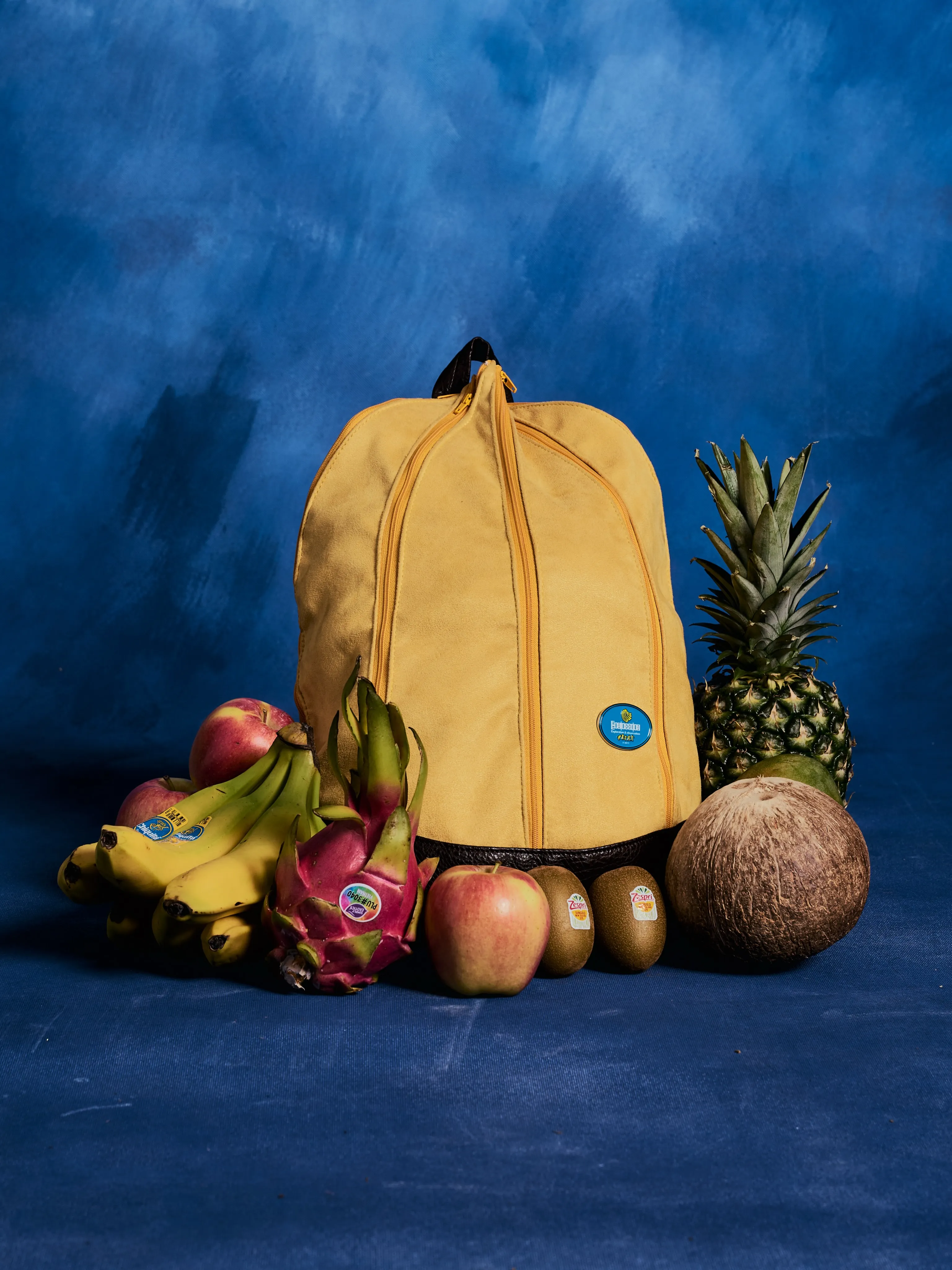 The Banackpack standing on a blue studio backdrop surrounded by fruit